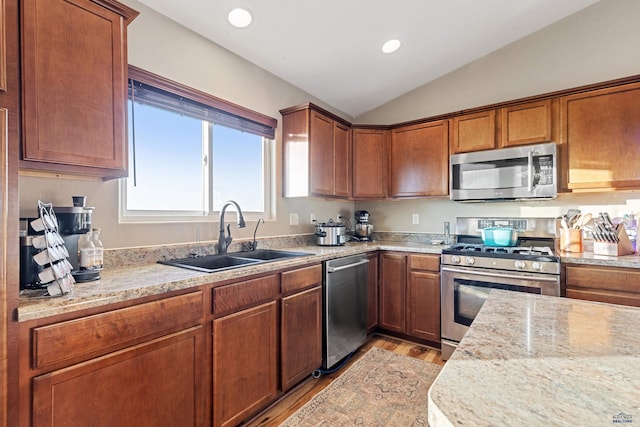 kitchen featuring lofted ceiling, light stone counters, stainless steel appliances, light wood-type flooring, and a sink