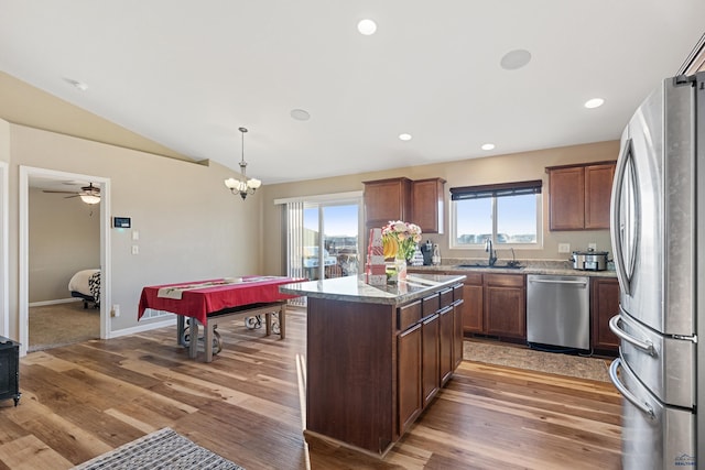 kitchen featuring a sink, a kitchen island, vaulted ceiling, hanging light fixtures, and appliances with stainless steel finishes