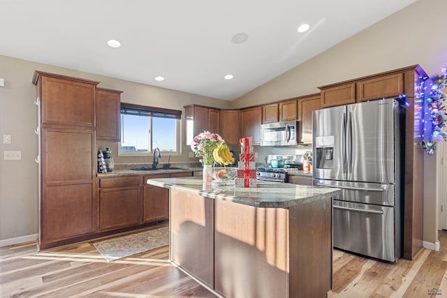 kitchen featuring lofted ceiling, appliances with stainless steel finishes, a sink, a kitchen island, and dark stone countertops