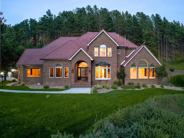 view of front of property featuring brick siding, a tile roof, a wooded view, and a front yard