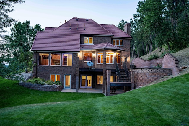 rear view of property with a patio, a chimney, stairs, a yard, and brick siding