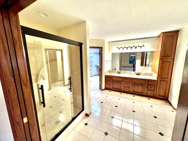 bathroom featuring double vanity, a stall shower, a sink, a textured ceiling, and baseboards