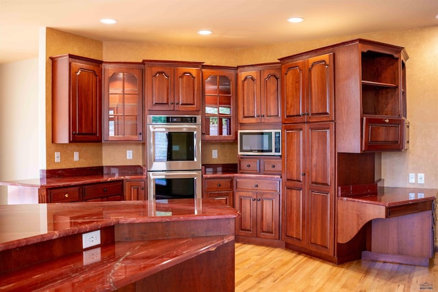 kitchen featuring light wood finished floors, stone countertops, glass insert cabinets, appliances with stainless steel finishes, and recessed lighting