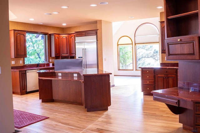 kitchen with light wood-style flooring, recessed lighting, stainless steel appliances, a kitchen island, and dark countertops