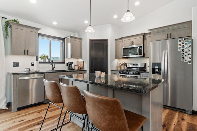 kitchen with a center island, decorative light fixtures, appliances with stainless steel finishes, a sink, and dark stone countertops