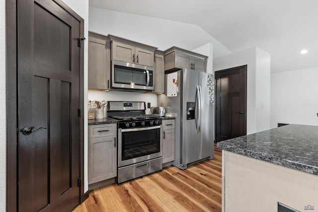 kitchen featuring vaulted ceiling, appliances with stainless steel finishes, gray cabinets, dark stone counters, and light wood finished floors