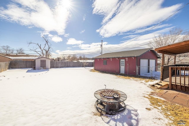 yard covered in snow featuring a fire pit, a shed, an outdoor structure, and a fenced backyard