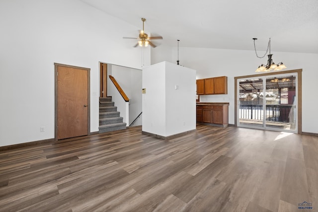 unfurnished living room with stairway, dark wood-type flooring, high vaulted ceiling, baseboards, and ceiling fan with notable chandelier