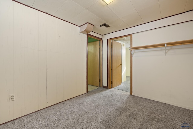 unfurnished bedroom with light colored carpet, visible vents, and wood walls