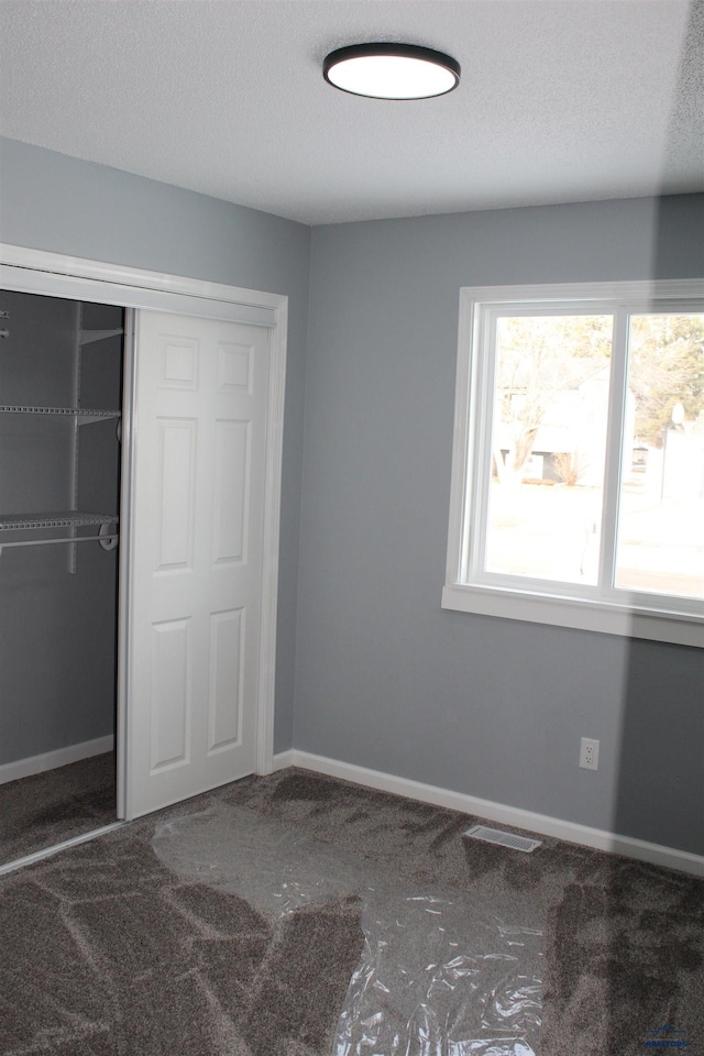 unfurnished bedroom featuring a closet, carpet flooring, a textured ceiling, and baseboards