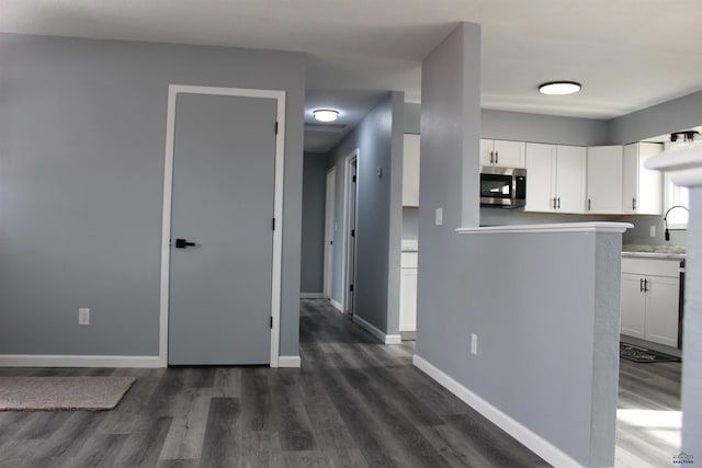 kitchen featuring baseboards, white cabinets, stainless steel microwave, dark wood-type flooring, and light countertops