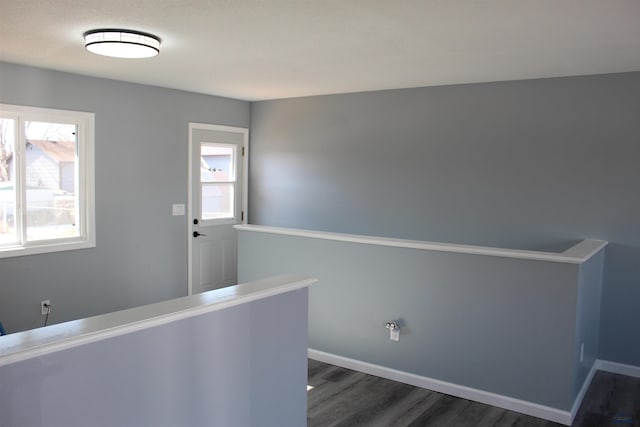 hallway with a healthy amount of sunlight, dark wood-style floors, baseboards, and an upstairs landing