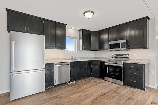 kitchen with light wood-style flooring, appliances with stainless steel finishes, light countertops, and dark cabinetry