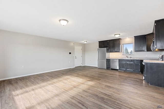 kitchen featuring open floor plan, wood finished floors, stainless steel appliances, light countertops, and a sink