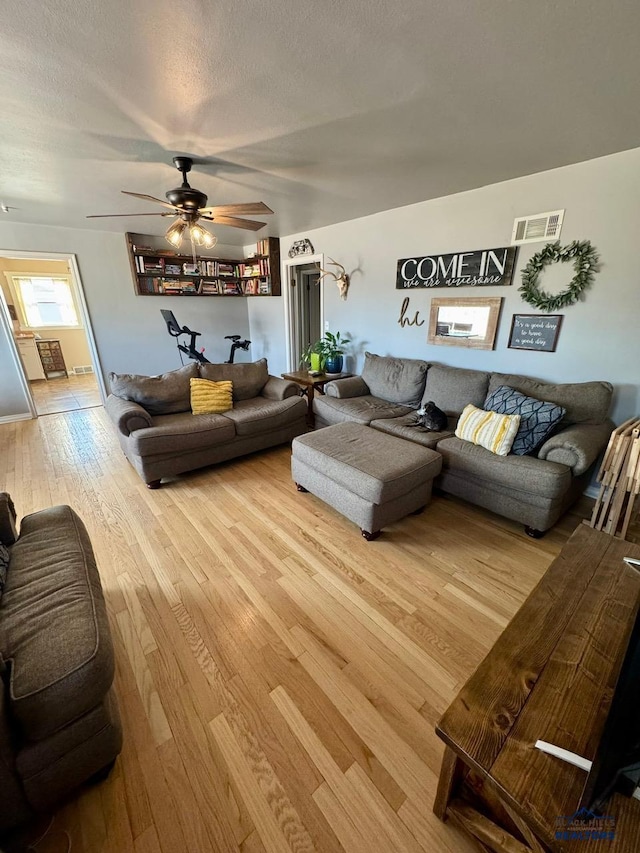 living room with light wood-style floors, ceiling fan, visible vents, and a textured ceiling