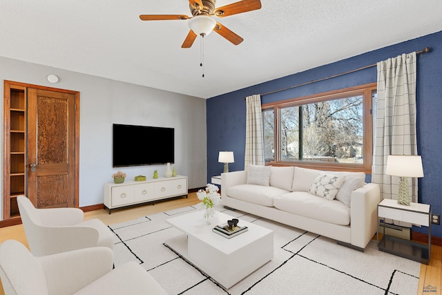 living room with light wood-style floors, ceiling fan, a textured ceiling, and baseboards