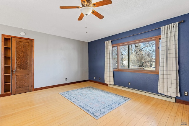 empty room with a textured ceiling, a baseboard heating unit, wood finished floors, a ceiling fan, and baseboards