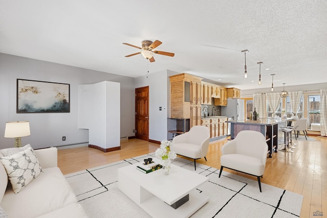 living room featuring baseboard heating, light wood-style floors, ceiling fan, a textured ceiling, and baseboards