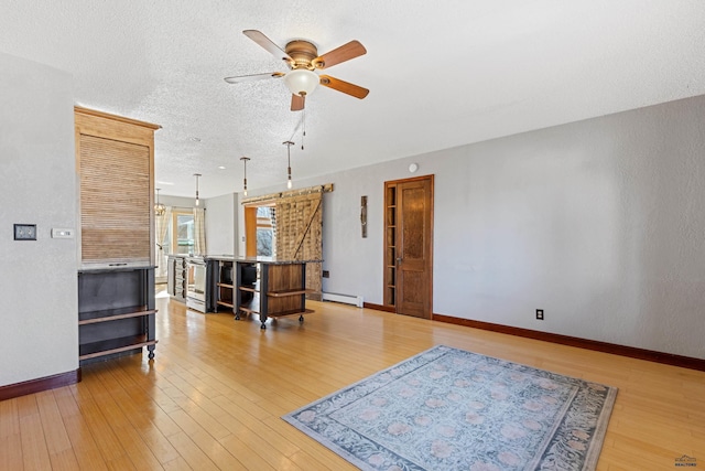 living area with light wood finished floors, baseboards, baseboard heating, and a textured ceiling