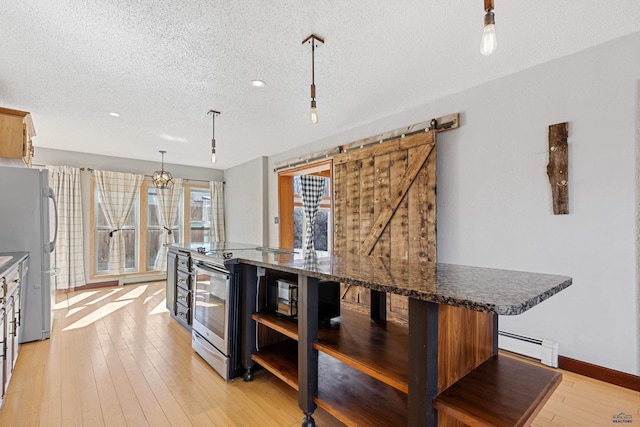 kitchen with stainless steel appliances, decorative light fixtures, dark stone countertops, and a barn door