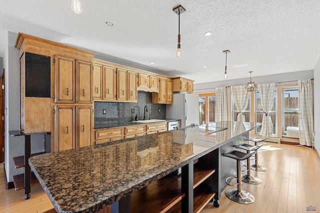 kitchen featuring decorative light fixtures, a breakfast bar area, freestanding refrigerator, a sink, and dark stone counters