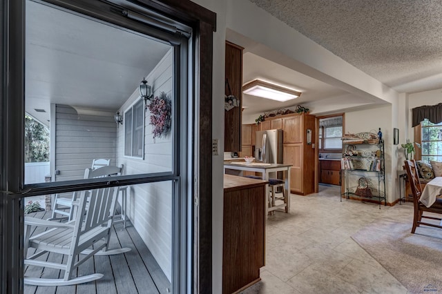 interior space with brown cabinetry, a textured ceiling, and stainless steel fridge with ice dispenser