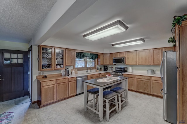 kitchen with stainless steel appliances, a sink, light countertops, brown cabinets, and glass insert cabinets