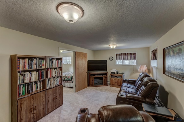 living room featuring a textured ceiling, a glass covered fireplace, a wealth of natural light, and light colored carpet