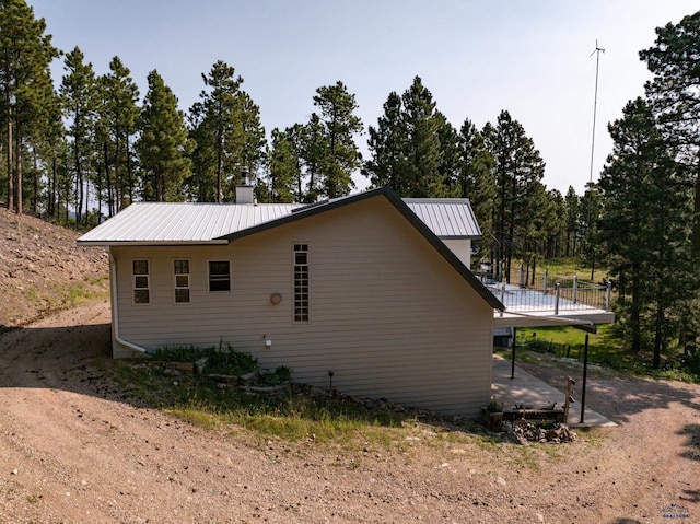 view of property exterior featuring metal roof, a chimney, and a wooden deck