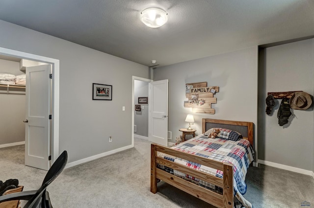 bedroom with a walk in closet, light colored carpet, a textured ceiling, and baseboards