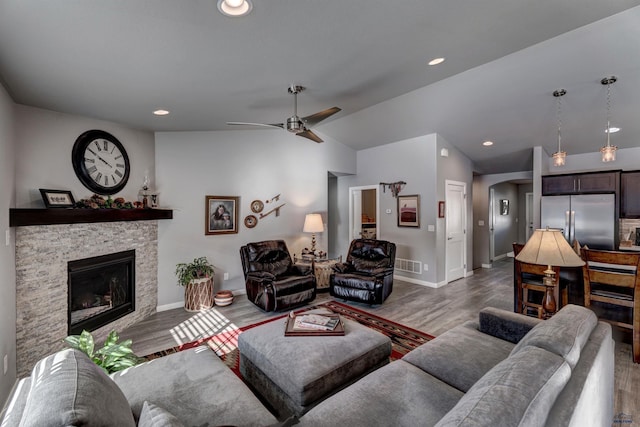 living room featuring visible vents, arched walkways, lofted ceiling, wood finished floors, and a fireplace