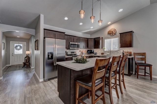 kitchen with arched walkways, light countertops, appliances with stainless steel finishes, a center island, and pendant lighting