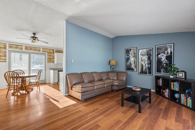 living area with lofted ceiling, a textured ceiling, a ceiling fan, and wood finished floors