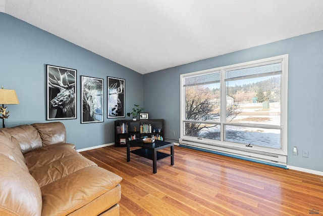 living area featuring lofted ceiling, baseboard heating, wood finished floors, and baseboards