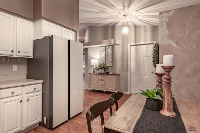 kitchen featuring light countertops, hanging light fixtures, light wood-style floors, freestanding refrigerator, and white cabinets