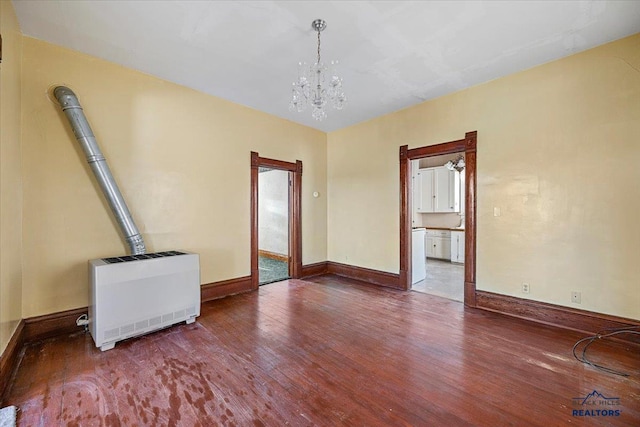 unfurnished living room with an inviting chandelier, baseboards, heating unit, and wood finished floors