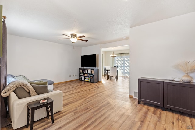 living area with a textured ceiling, light wood-style flooring, ceiling fan with notable chandelier, visible vents, and baseboards