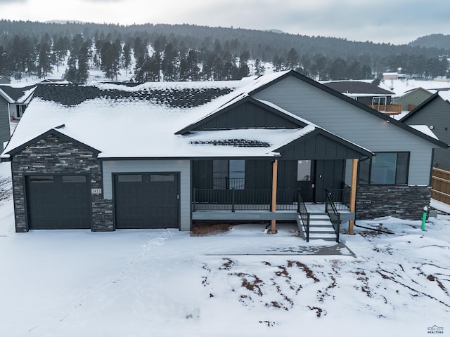 view of front facade with an attached garage, stone siding, a view of trees, and board and batten siding