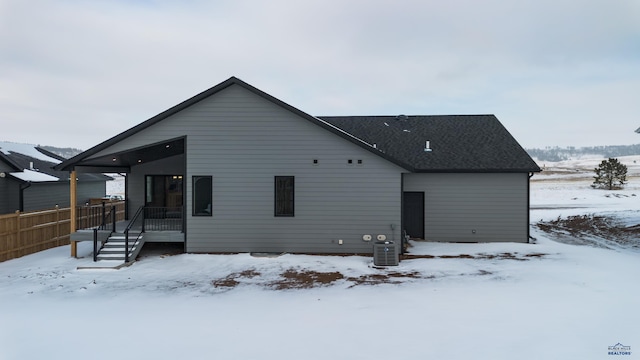 snow covered rear of property featuring fence and central AC