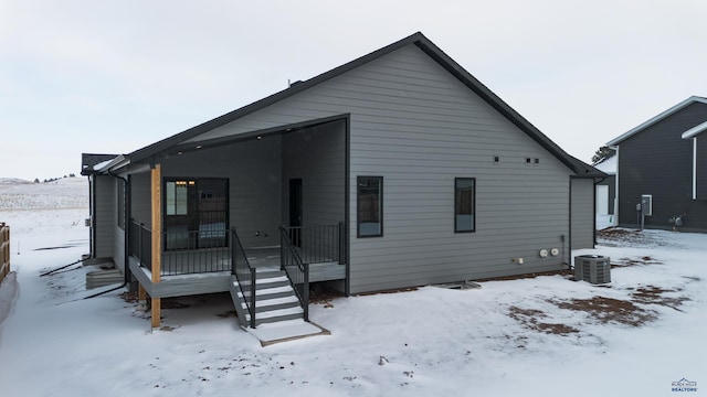 snow covered back of property with a garage, covered porch, and cooling unit