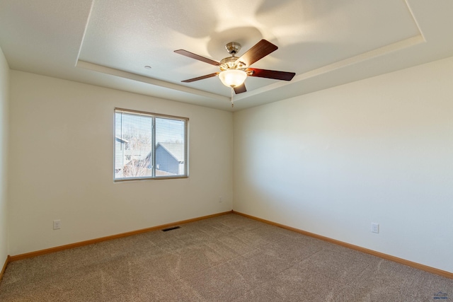 empty room featuring a tray ceiling, visible vents, and light carpet