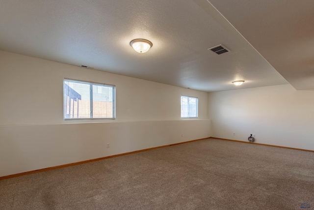 carpeted spare room with baseboards, visible vents, and a textured ceiling