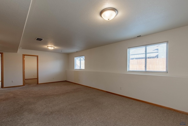 empty room featuring light carpet, visible vents, baseboards, and a textured ceiling