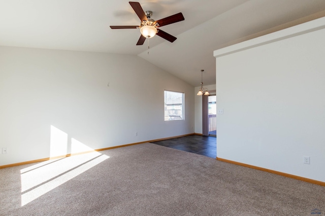 spare room with vaulted ceiling, ceiling fan with notable chandelier, dark carpet, and baseboards