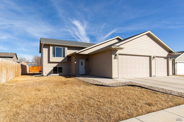 split level home with a garage, concrete driveway, a front lawn, and fence