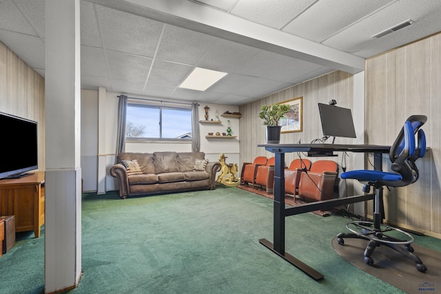 carpeted office with visible vents, wood walls, and a drop ceiling