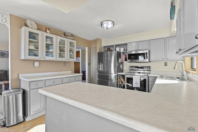 kitchen with stainless steel appliances, light countertops, glass insert cabinets, a sink, and a peninsula