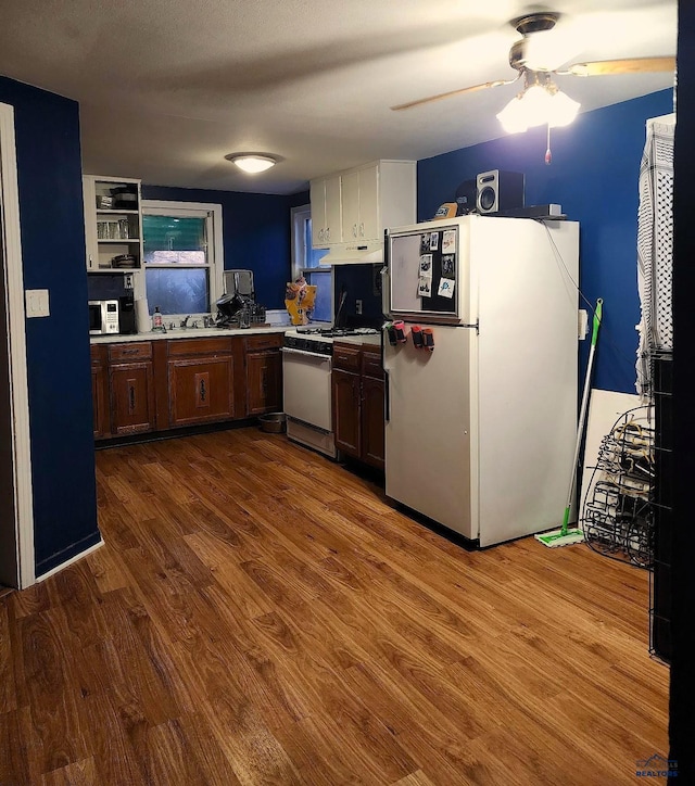 kitchen featuring under cabinet range hood, white appliances, dark wood-style flooring, a sink, and light countertops