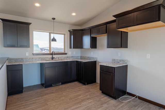 kitchen with light wood finished floors, recessed lighting, vaulted ceiling, a sink, and dark brown cabinets