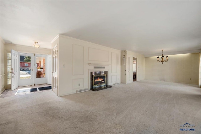 unfurnished living room featuring carpet flooring, visible vents, ornamental molding, a glass covered fireplace, and an inviting chandelier